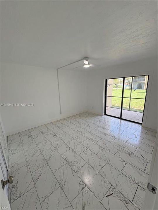 Interior space featuring large-format veined tile flooring, a ceiling fan with integrated lighting, and sliding glass doors leading to a screened-in patio