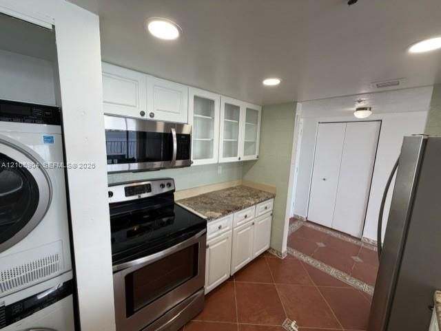 Kitchen featuring white cabinetry with glass-panel upper doors, stone-surface countertops, stainless steel appliances, and tiled flooring
