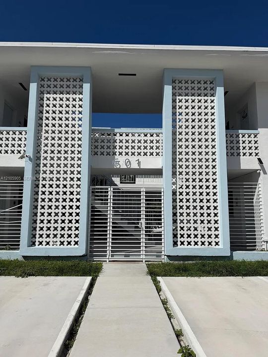 Mid-century modern exterior featuring decorative white concrete breeze blocks, two-story facade with structured columns, and a secure metal gate entryway
