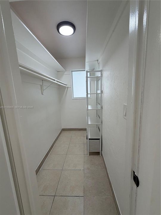 Walk-in closet featuring ceramic tile flooring, built-in shelving, a full-width hanging rod, and a central ceiling light fixture
