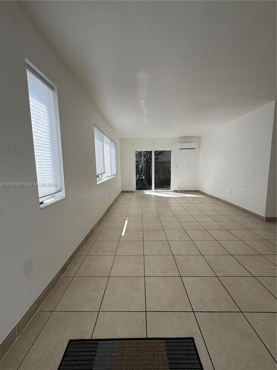 Neutral-toned ceramic tile flooring, sliding glass door, wall-mounted ductless climate control unit, and window treatments