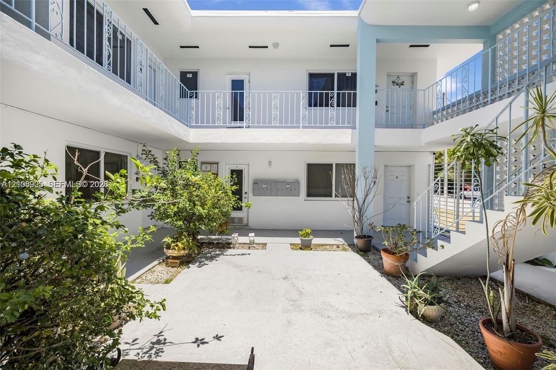 Open-air courtyard featuring white stucco exterior walls, two-story metal railings, an external staircase, and integrated planter beds