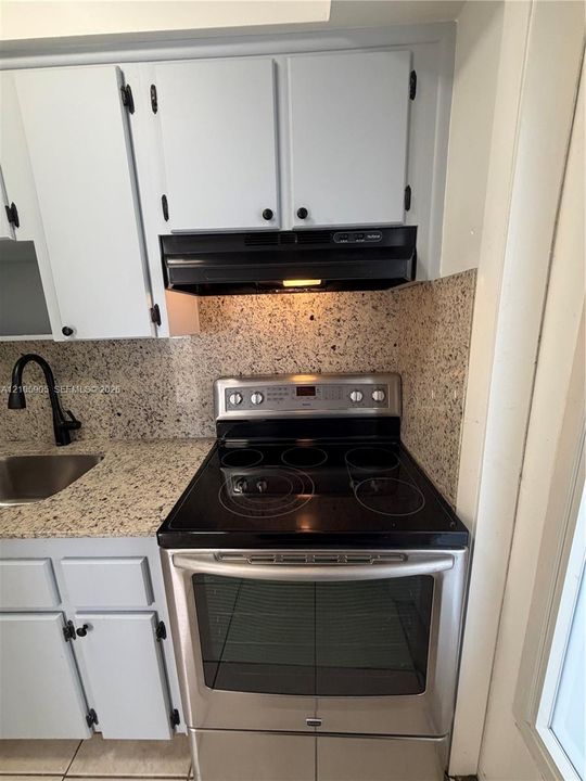 Kitchen featuring light-toned cabinetry, stone-finish countertops, a stainless steel electric range, a black range hood, and a dark-finish faucet