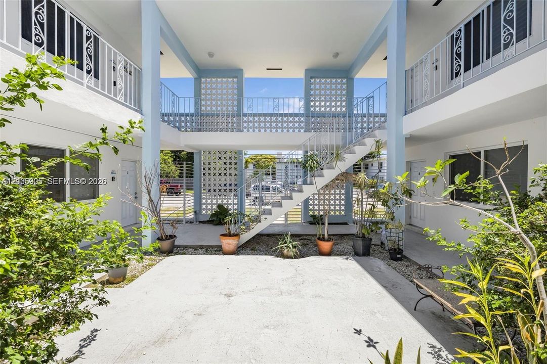 Exterior courtyard featuring mid-century inspired breeze block screens, open-air stairwell, metal railings, and a concrete patio