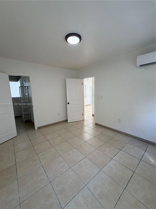 Neutral interior space featuring tile flooring, white paneled doors, and a wall-mounted ductless climate control unit
