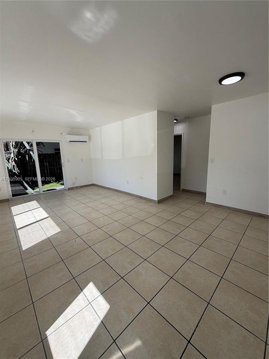 Interior space featuring neutral tile flooring, sliding glass door, wall-mounted air conditioning unit, and recessed ceiling lighting