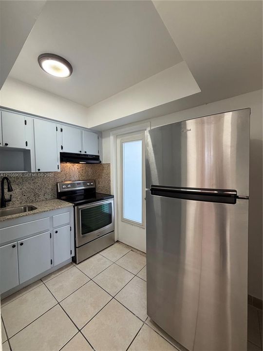 Kitchen featuring stainless steel appliances, stone-finish countertops, tiled flooring, built-in cabinetry, and a flush-mount ceiling light