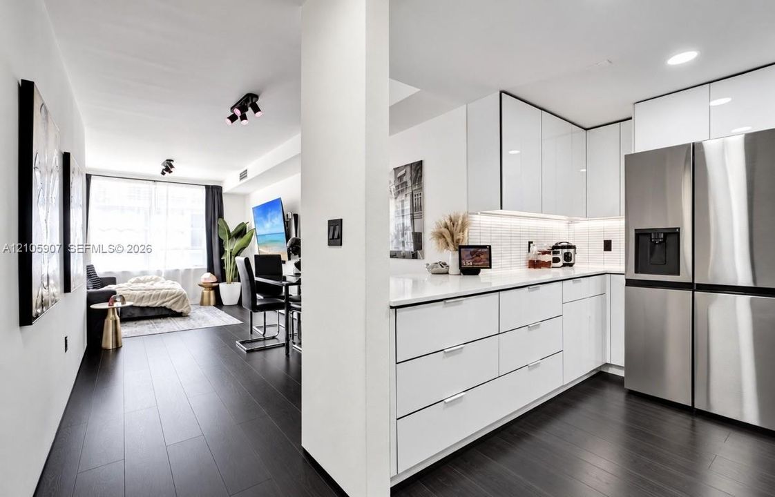Kitchen featuring white cabinetry with flat-panel doors, quartz countertops, white tile backsplash, stainless steel refrigerator, and dark wood-finish flooring
