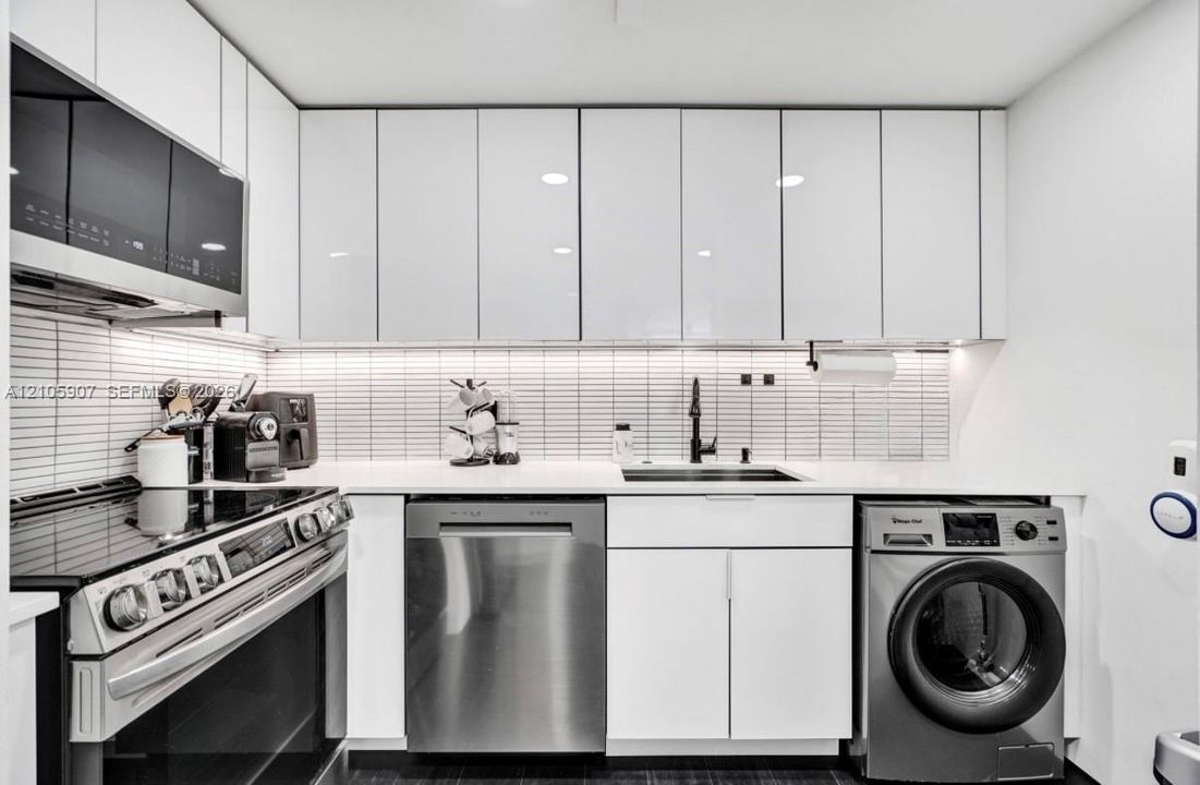 Sleek kitchen featuring high-gloss white cabinetry, linear tiled backsplash, integrated stainless steel appliances, solid surface countertops, and under-cabinet lighting
