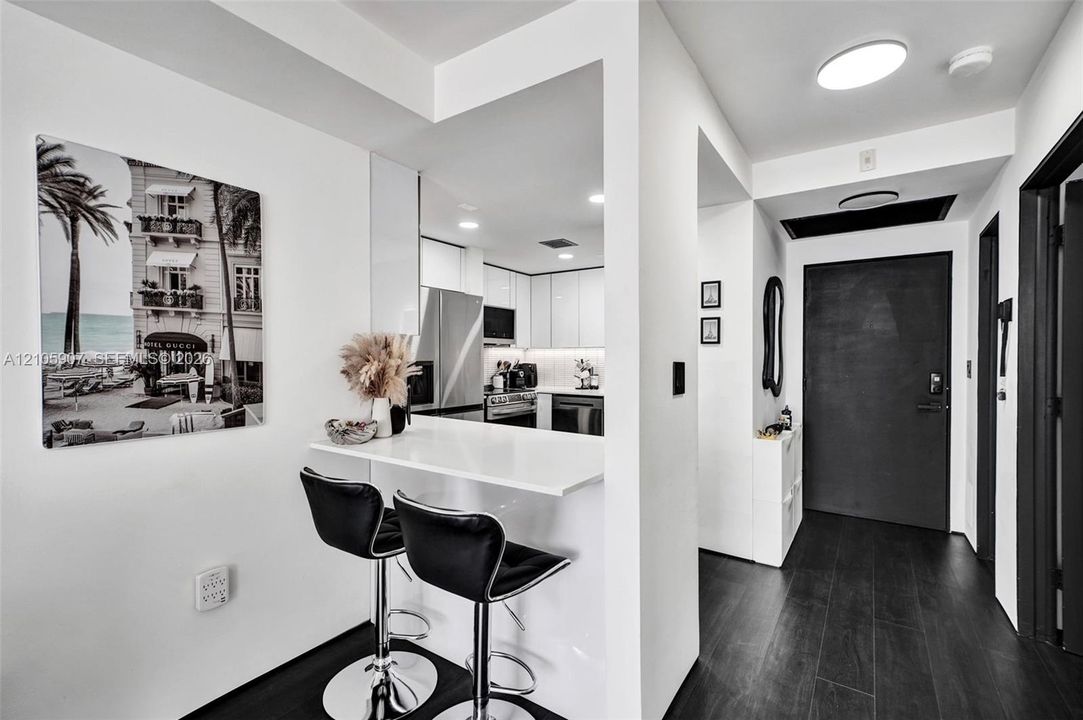 Interior entry featuring dark wood-finish flooring, a built-in white peninsula counter, flat-panel white cabinetry, and stainless steel appliances