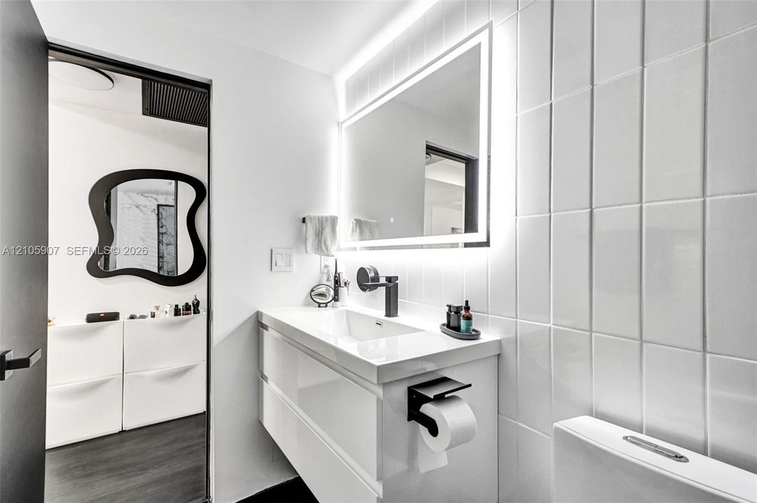 Wall-mounted floating vanity with integrated rectangular sink, matte black wall-mounted faucet, rectangular LED-backlit mirror, and vertical glossy white wall tile