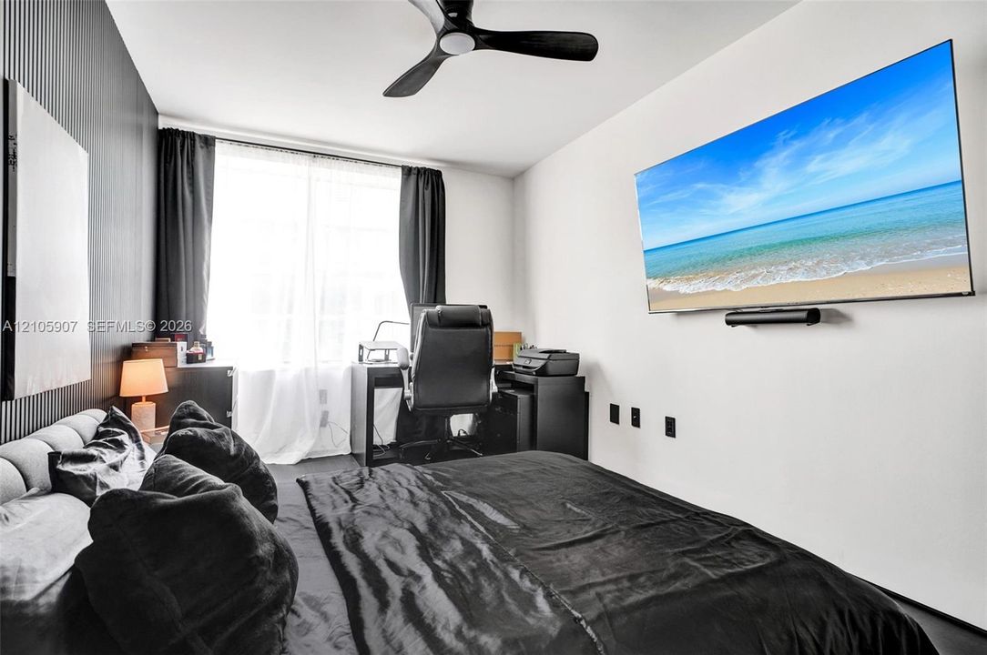 Room featuring a matte black vertical-slat accent wall, three-blade ceiling fan, and large window with natural light