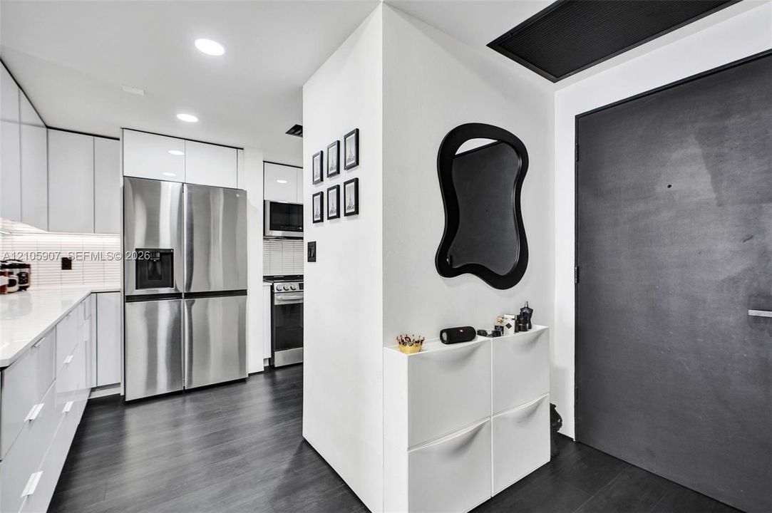 Contemporary kitchen featuring high-gloss white cabinetry, stainless steel appliances, integrated microwave, and dark-toned flooring