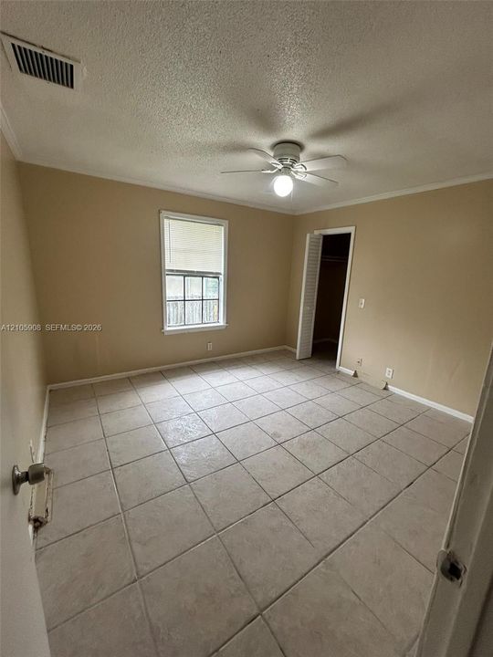 Interior room featuring large-format ceramic tile flooring, a multi-blade ceiling fan with center light, a single-hung window, and a built-in closet with louvered folding doors