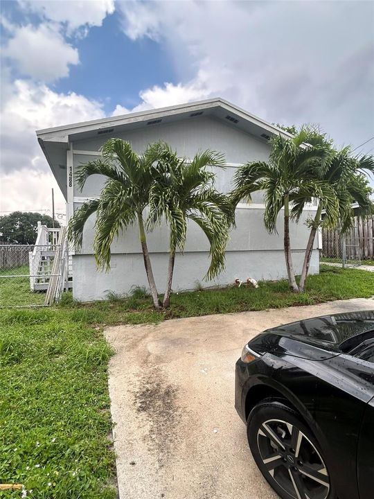 Single-story residence featuring a gabled roofline, concrete driveway, attached staircase with metal railings, and mature palm trees