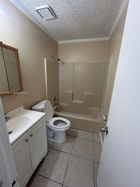 Bathroom featuring a white vanity cabinet with a integrated sink, molded tub and shower surround, and tile flooring