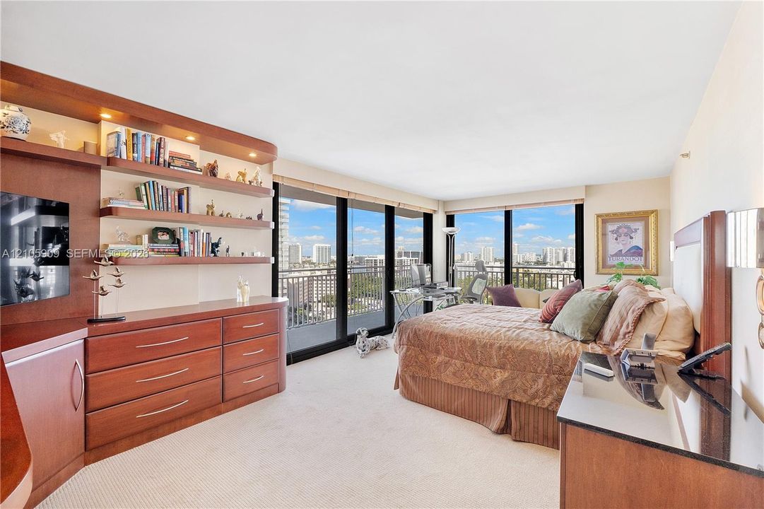 Custom wood-finish built-in cabinetry with integrated shelving, floor-to-ceiling glass sliding doors, and expansive urban scenery