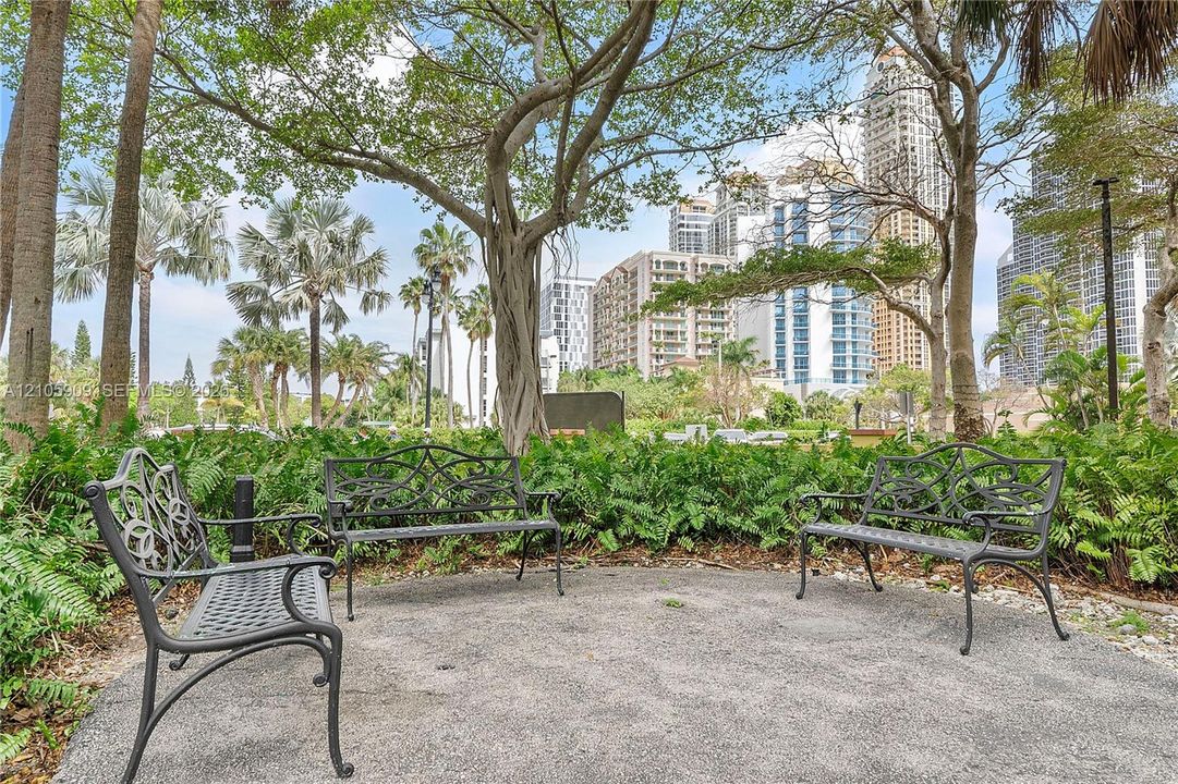 Landscaped grounds featuring crushed stone pathways, mature native trees, tropical foliage, and decorative wrought-iron benches