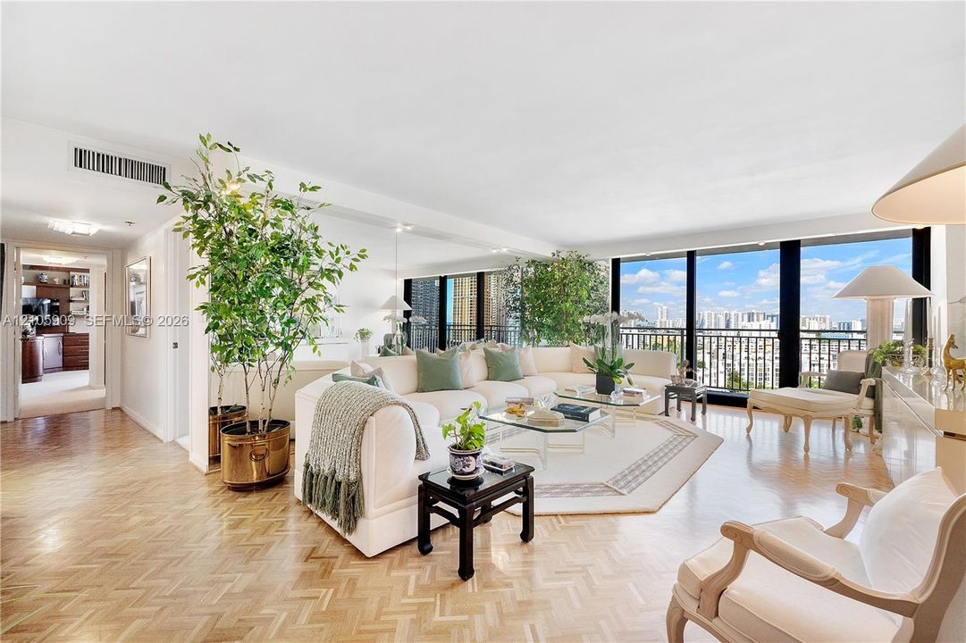 Expansive living area featuring herringbone-pattern wood flooring, floor-to-ceiling windows, an integrated mirrored wall, and a private balcony