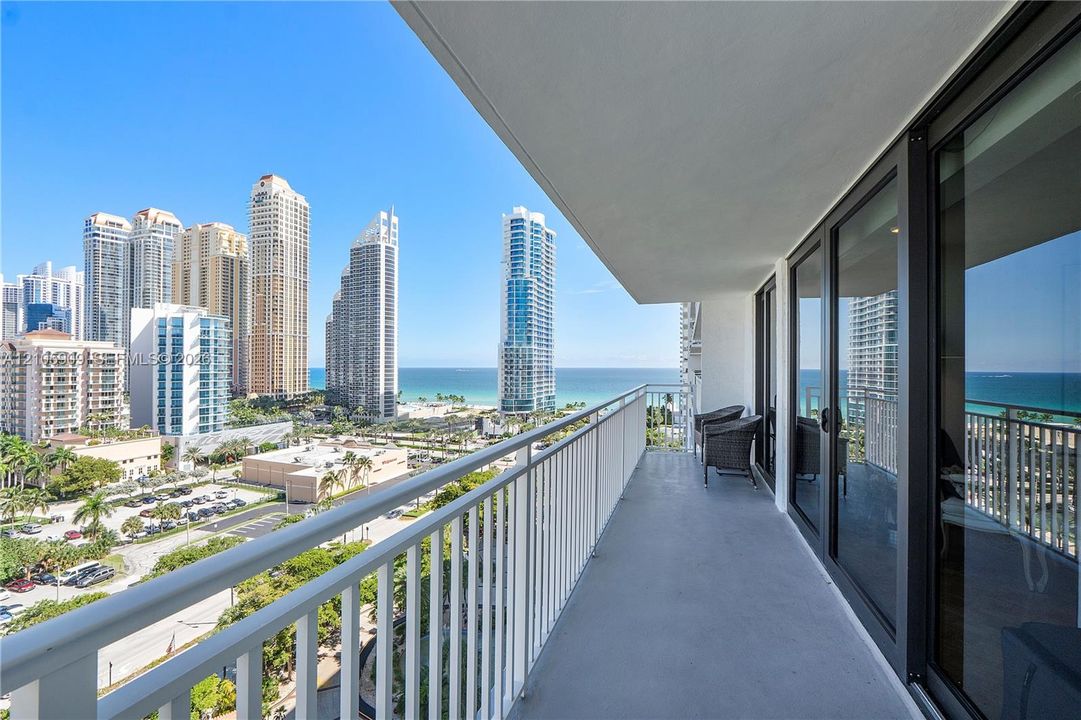Private balcony with metal railing, floor-to-ceiling glass sliding doors, and coastal cityscape backdrop