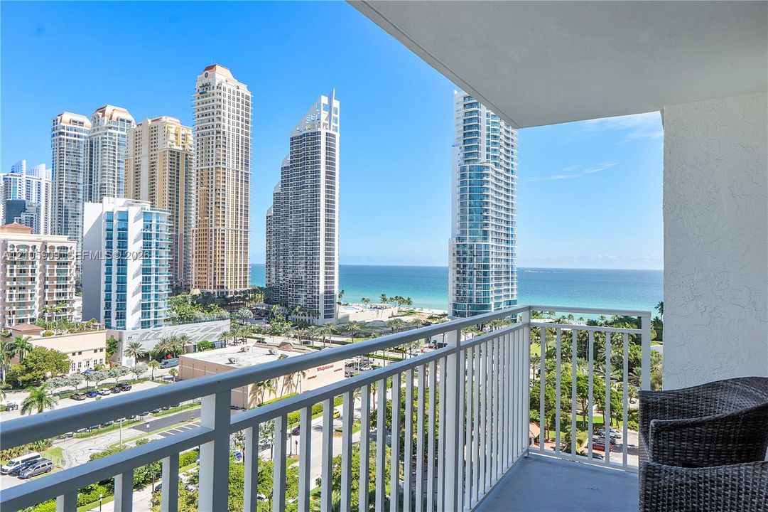 Private balcony with white metal railings, overlooking coastal scenery, ocean, and urban architecture