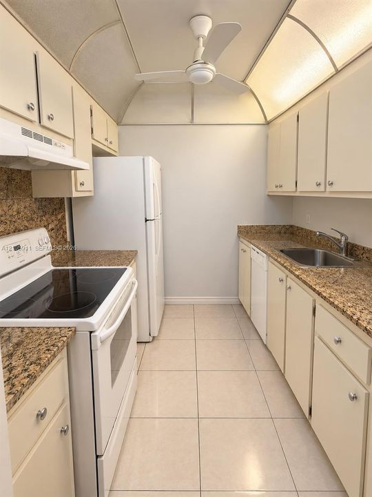 Kitchen featuring stone countertops, white cabinetry, integrated range, stainless steel sink, and vaulted ceiling with recessed lighting