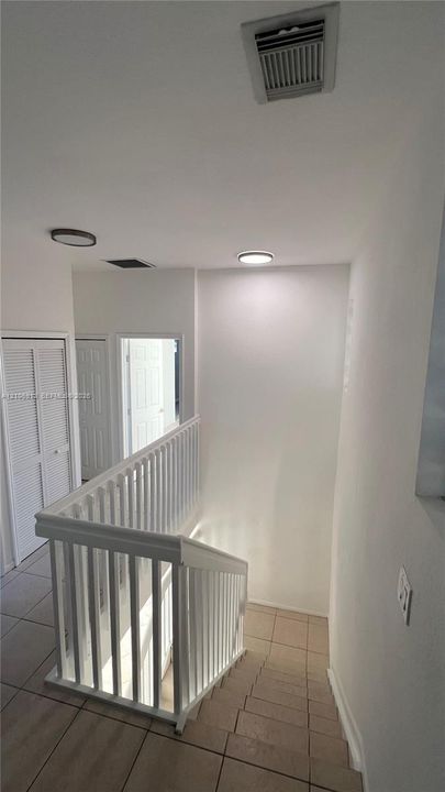 White wooden balustrade staircase featuring tile flooring and flush-mount lighting fixtures