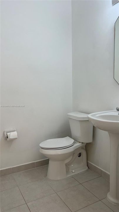 Pedestal sink, vitreous china toilet, and light-toned ceramic tile flooring