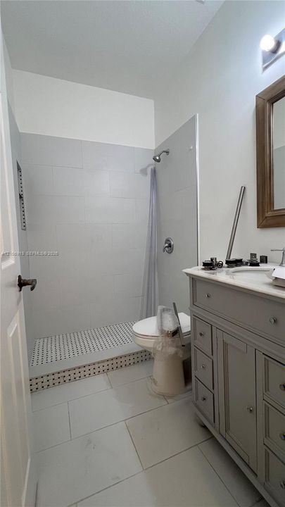 Bathroom featuring a vanity with shaker-style cabinetry, a walk-in shower with large-format tile surround, patterned tile shower floor, and large-format floor tiling