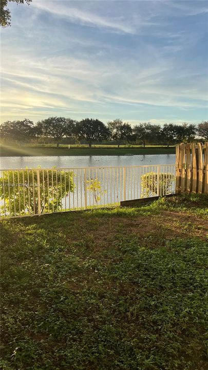 Waterfront backyard featuring a metal perimeter fence, grass lawn, and mature trees