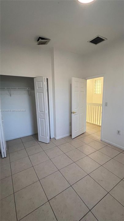 Neutral-toned ceramic tile flooring, interior six-panel doors, and built-in closet shelving