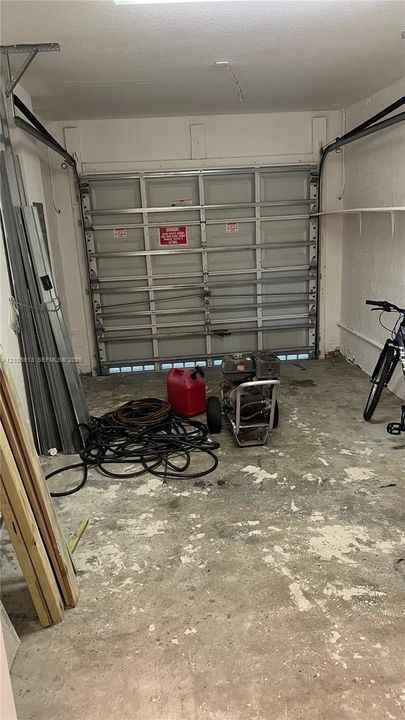 Garage space featuring a metal sectional door, overhead garage door mechanism, and white finished walls