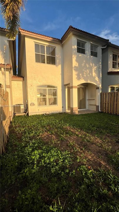 Two-story exterior featuring light-toned stucco siding, a tiled roof, a covered patio area, and enclosed wooden perimeter fencing