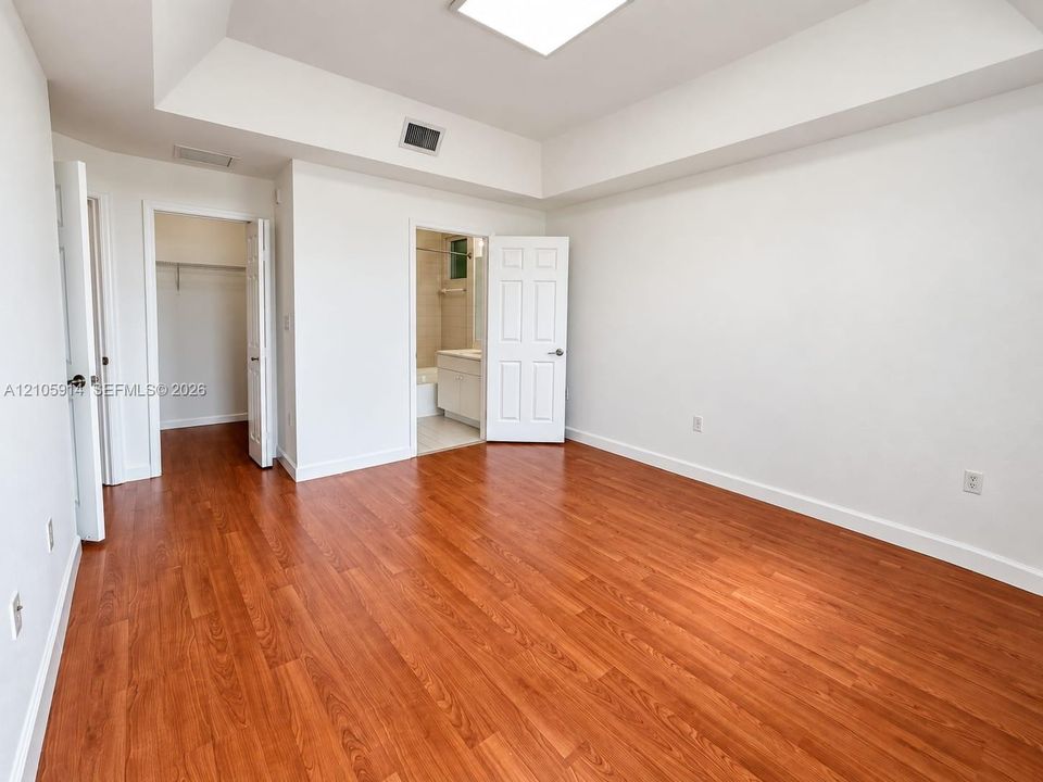 Room featuring wood-finish flooring, a tray ceiling, recessed lighting, and dual entry points to a walk-in closet and an en-suite bathroom