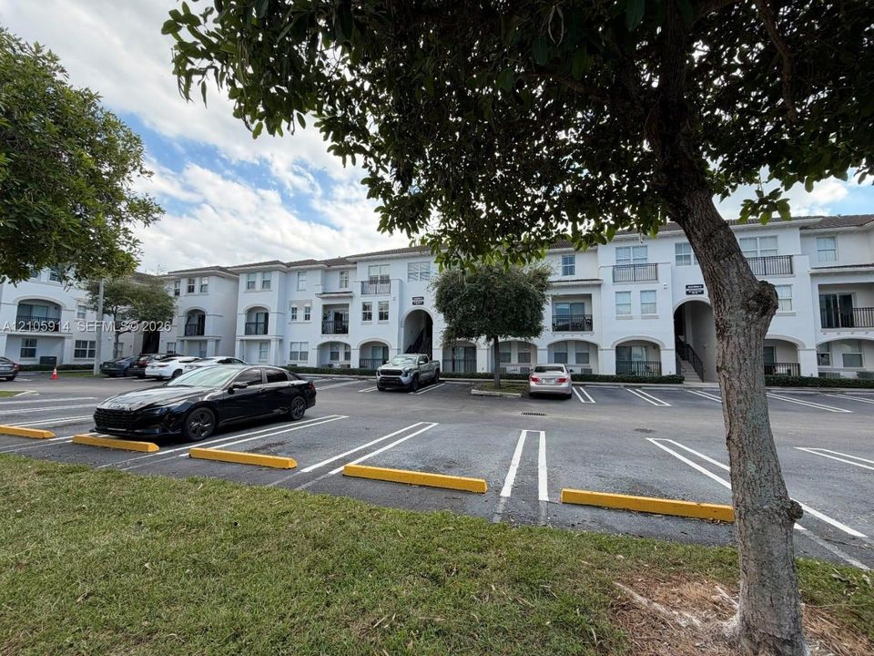 Multi-story residential complex featuring arched architectural details, private balconies, paved parking, and manicured landscaping