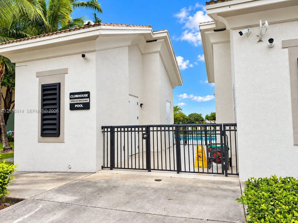Stucco exterior clubhouse featuring a gated entry, tiled roof, and decorative louvered shutter
