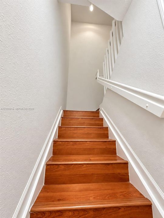 Staircase featuring wood-finish treads, white painted walls, and a white handrail with vertical balusters