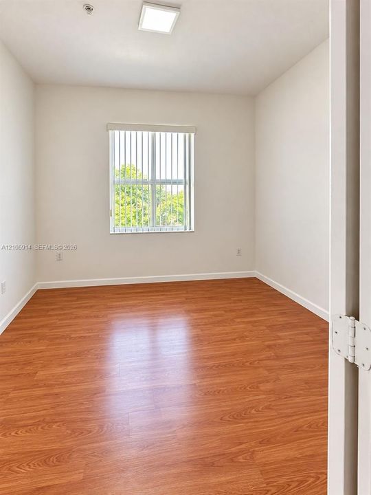 Interior space featuring wood-finish flooring, a neutral color palette, a rectangular window with vertical blinds, and a recessed ceiling light fixture