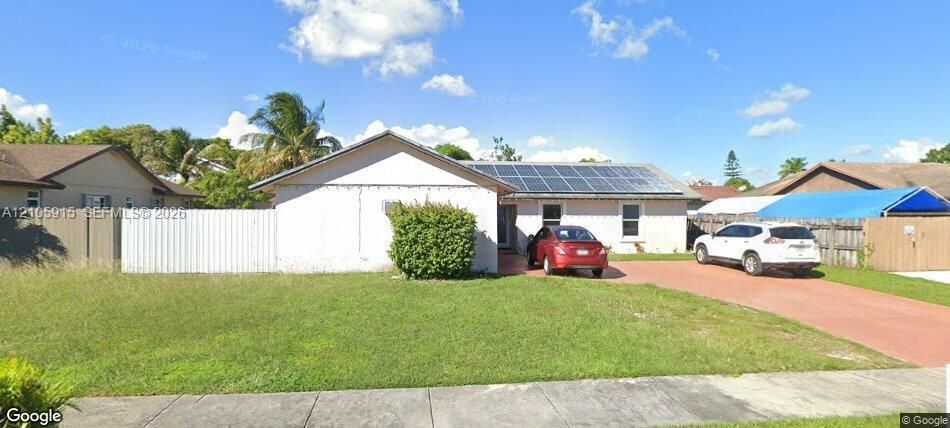 Single-story residence featuring a gable roof with integrated solar panels, concrete driveway, and white vinyl privacy fencing