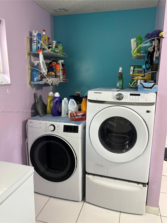 Laundry area featuring a front-loading washer and dryer, tile flooring, and wall-mounted wire shelving