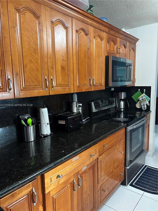 Kitchen cabinetry with arched detailing, dark stone countertops, integrated stainless steel microwave, stainless steel electric range, and tile flooring