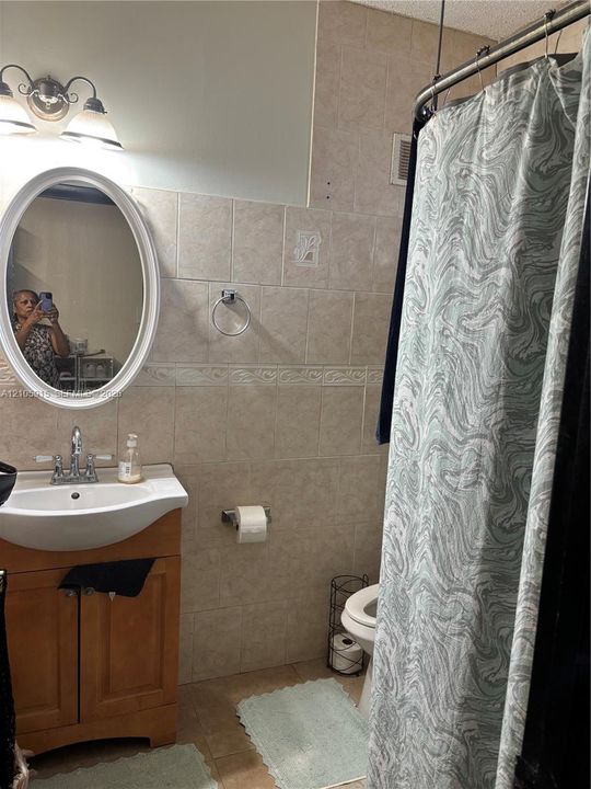 Wall-mounted oval mirror, wood-finish vanity cabinet, pedestal-style sink basin, two-light fixture, and ceramic tile wall finishes