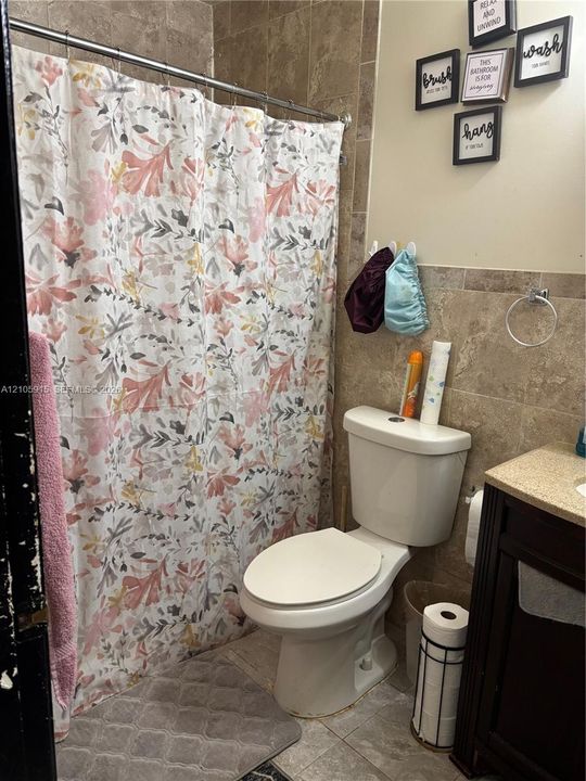 Bathroom featuring a tub-shower combination with full-height stone-finish wall tile, dark-finish wood cabinetry, and a stone-finish vanity countertop