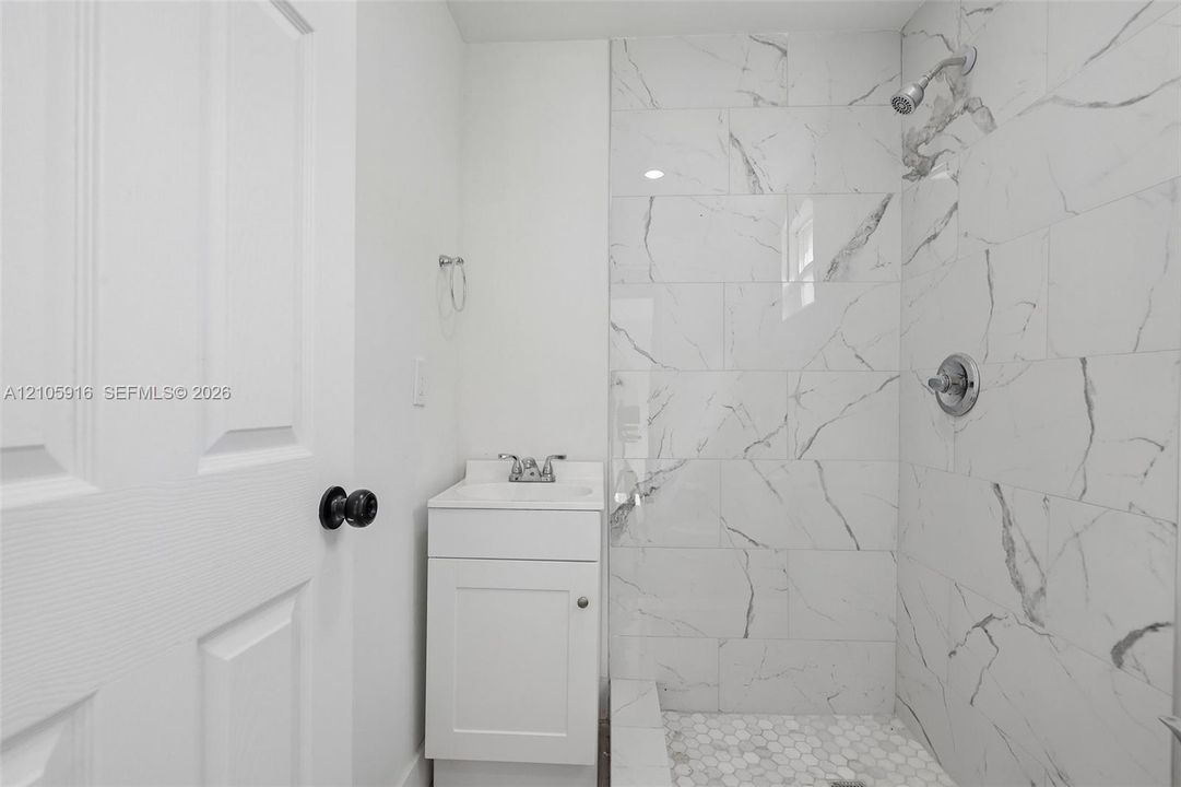 Bathroom featuring a white vanity cabinet, rectangular sink, shower enclosure with large-format veined tile surround, and hexagonal tile shower flooring
