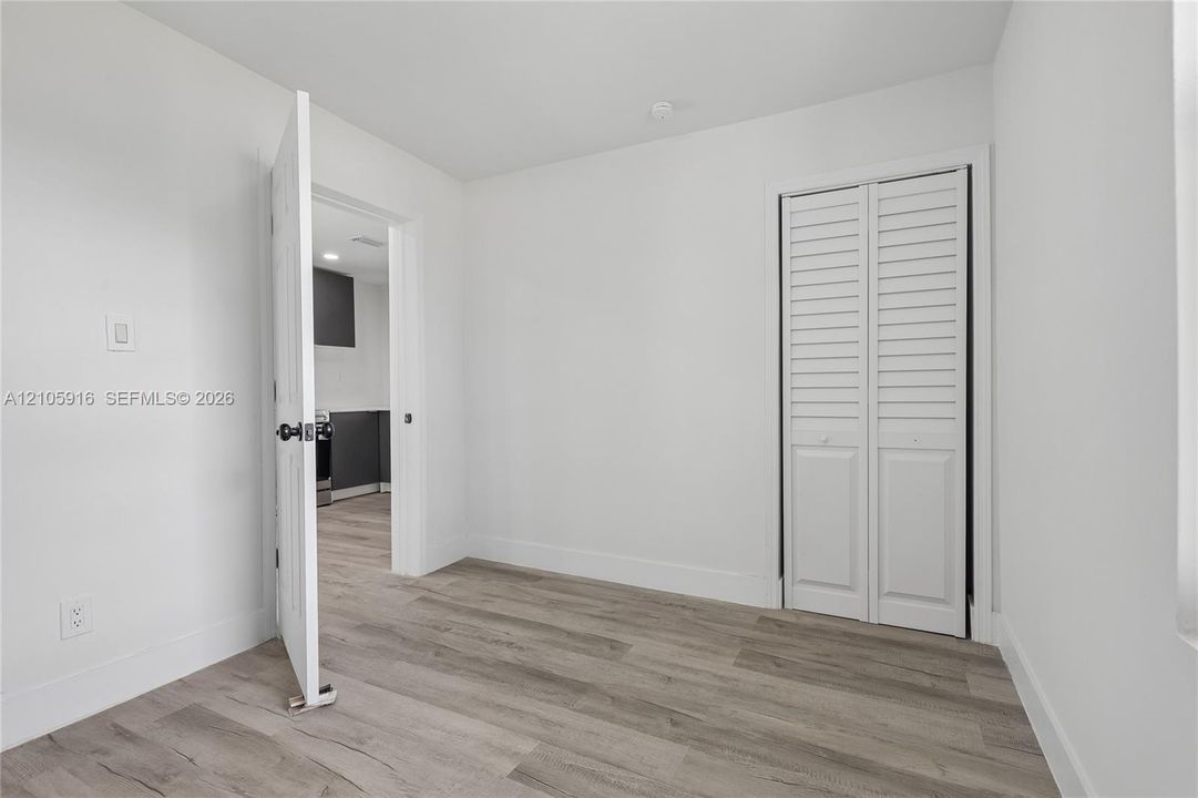 Neutral interior space featuring wood-finish flooring, white walls, and a closet with white louvered bifold doors