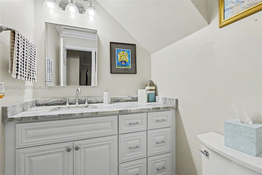 Bathroom vanity featuring white cabinetry, stone-patterned countertop, integrated sink, polished metal faucet, and wall-mounted three-light fixture