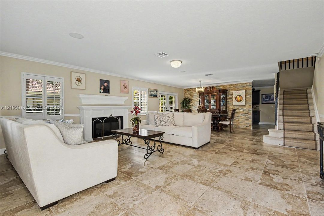 Living area featuring tile flooring, a fireplace with a white mantel, stone-accented wall, and a staircase with a runner