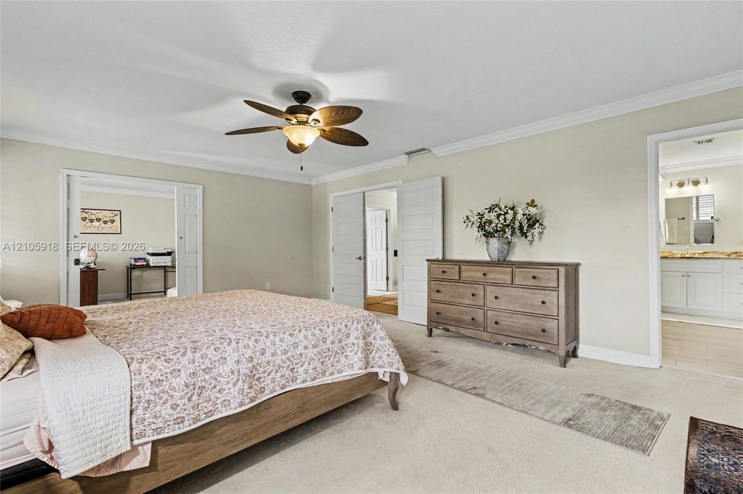 Neutral-toned room featuring a ceiling fan with integrated lighting, crown molding, and double-door entry