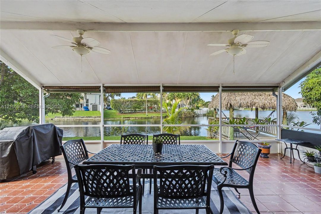 Screened-in covered patio featuring terracotta-style tile flooring, dual ceiling fans, and direct water access with a private wooden dock