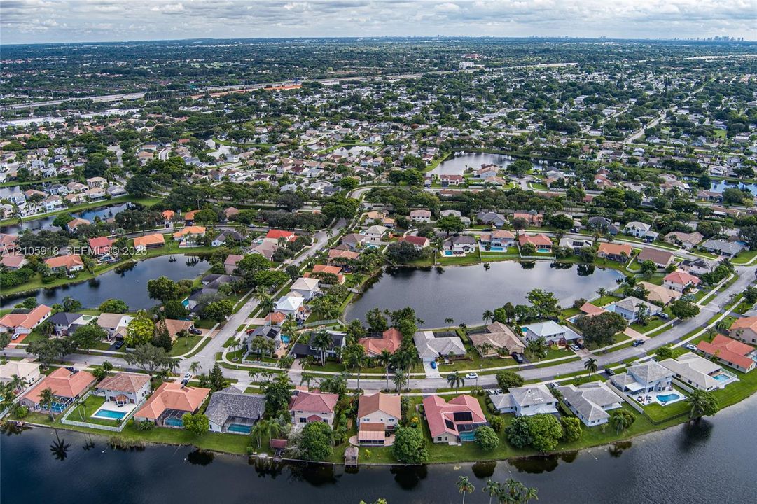 Aerial perspective of a residential community featuring winding paved streets, single-family dwellings with tile roofing, mature landscaping, and multiple waterfront lots
